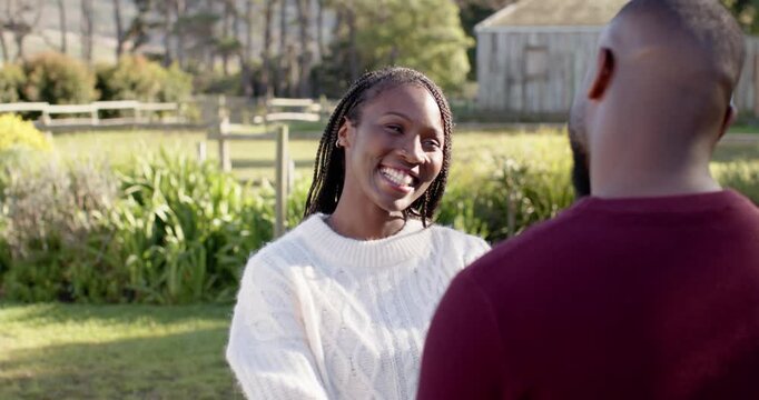 African couple in sunny yard woman in white knit smiling tilting urging man reaching holding hands