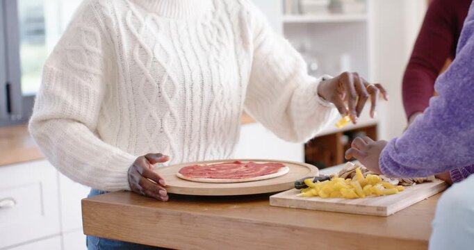 white knit steadying pizza board at counter, purple sleeve grabbing pepper mushrooms to top pizza