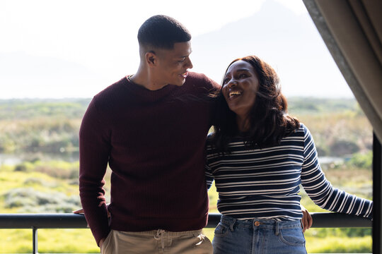 African American couple leaning on metal balcony rail, smiling, wearing knit sweater, striped top