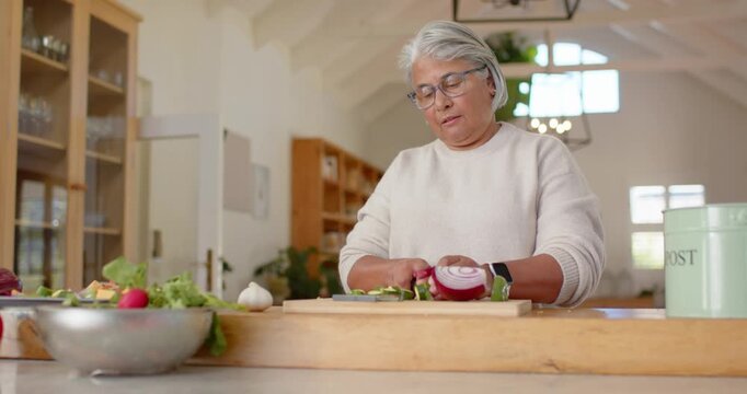 African American senior cook slicing onion, chopping greens, making salad in bowl at wooden island