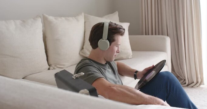 Man headphones on living room floor reaching case pulling vinyl inspecting label to play