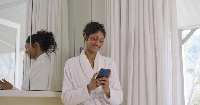 African American woman sitting on sink in robe holding phone taking selfies after applying patches