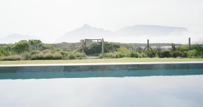 Light breeze is stirring pool water and moving grasses by wooden gate on dune, shifting haze