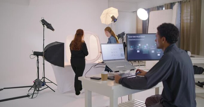 Diverse coworkers returning after adjusting light tent, reviewing Brand-Safe Check on monitors