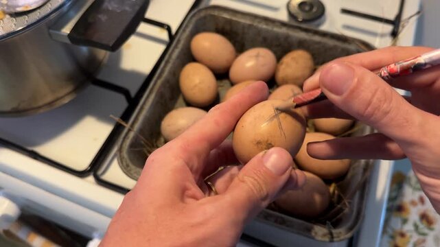 Hands picking up an egg and drawing a pencil cross on its shell