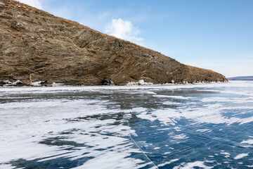 Clear blue ice with snow patches stretches along rocky shores under bright sky in Irkutsk Oblast, Russia, showing pristine natural winter scenery of frozen Lake Baikal in Siberia © TravelFlow