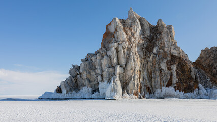 Scenic view of the famous Shamanka Rock surrounded by snowy ice on frozen Lake Baikal near Khuzhir village in Irkutsk Oblast, Russia during a bright sunny winter day with blue sky © TravelFlow