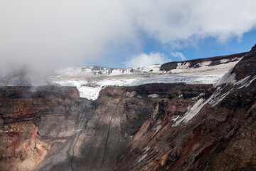 Rugged volcanic crater with layers of ancient ice and volcanic rock under clouds at Plosky Tolbachik volcano on the Kamchatka Peninsula in Russia, showcasing wild geological wilderness © TravelFlow