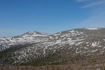 Scenic landscape of Mount Konzhakovsky Kamen in Sverdlovsk Oblast showing rocky slopes covered with snow patches and northern boreal forest under a clear blue sky in Russia © TravelFlow