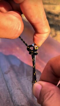 Hand tying black rope knot around metal nail on wooden table