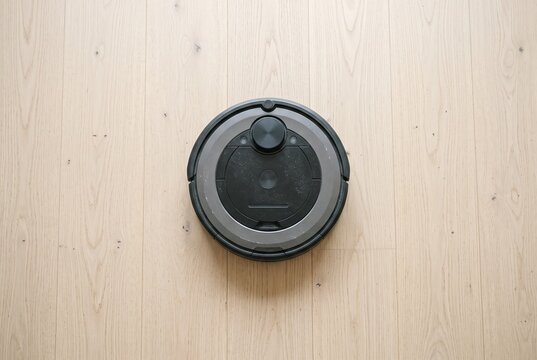 Unbranded robot vacuum seen from above on a wooden floor