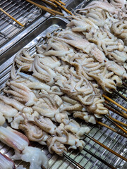 A dense pile of small pale octopus tentacles skewered on wooden sticks, heaped inside a stainless steel tray. © Suphattra