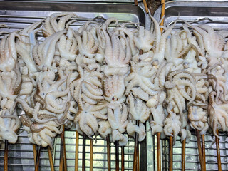 A dense pile of small pale octopus tentacles skewered on wooden sticks, heaped inside a stainless steel tray. © Suphattra