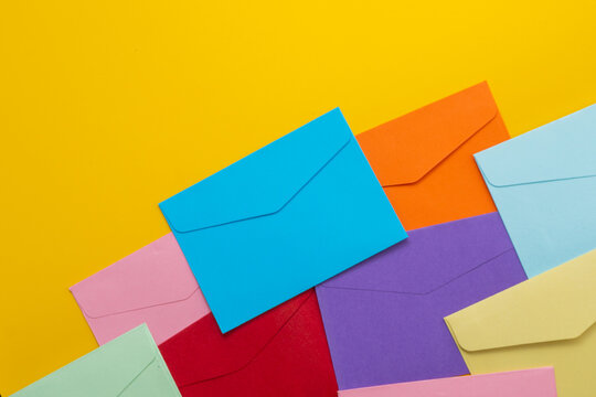 Flat lay of colorful paper envelopes on a yellow background with copy space. Direct marketing, business communication, and mail templates concept.