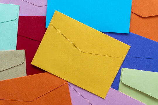 Flat lay of scattered colorful blank paper envelopes featuring a prominent yellow envelope in the center. Mail, direct marketing, newsletters, and business communication concept.