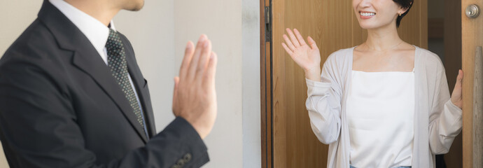 おしゃれで綺麗な新築一戸建ての緑あふれる玄関先で、仕事に出勤するスーツ姿の夫を笑顔で見送る日本人の妻、いってらっしゃいと挨拶する仲の良い夫婦の朝の暮らしと通勤風景上半身イメージ顔無しバナー © kapinon
