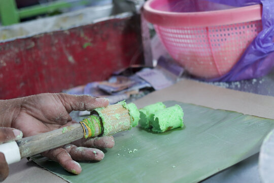 hand pushing a freshly steamed green putu bambu cake out of a bamboo tube