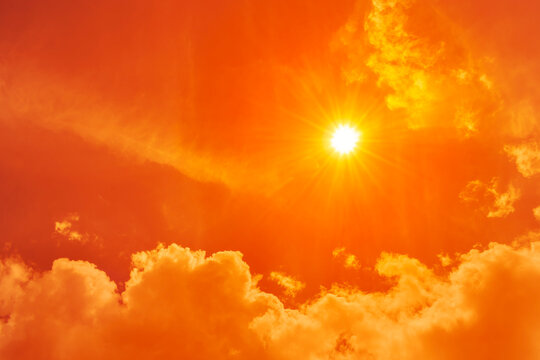 Intense sunlight shining through an orange sky with glowing clouds, representing extreme heat, heatwaves, global boiling, and climate change.