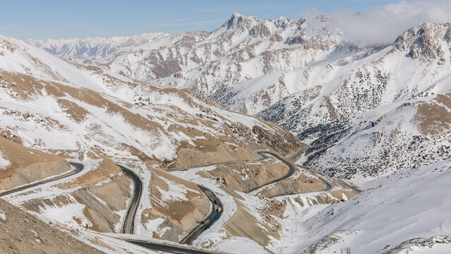 Winding asphalt highway curves through the scenic snow covered peaks of Taldyk Pass in Osh Region, Kyrgyzstan, creating an impressive highland route across dramatic terrain
