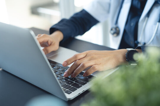 Close up of female doctor typing on laptop, working at medical clinic at desk