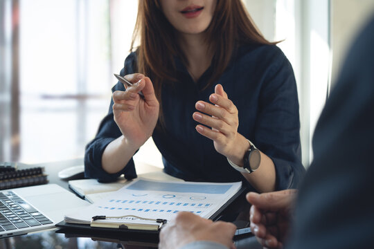 Businesswoman discussing financial charts with colleague at office desk, analyzing data and explaining strategy during a professional meeting.