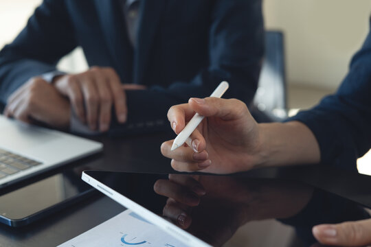 Close-up of businesswoman using stylus on digital tablet during meeting with colleague in office, modern technology and collaboration concept.
