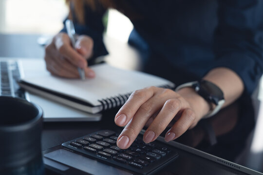 Doing finance, budgeting and tax calculation. Close up woman using calculator to calculate financial report, accounting with laptop on table, budget management