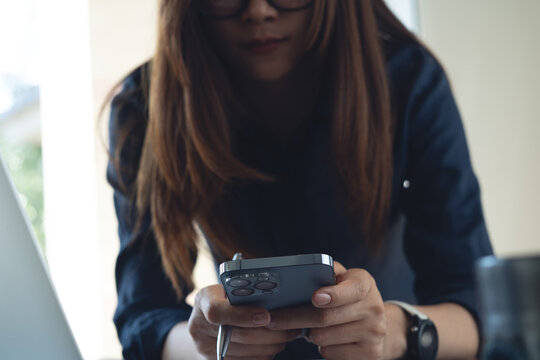 Close-up of businesswoman using smartphone while working at desk with laptop, modern business lifestyle, mobile technology concept.