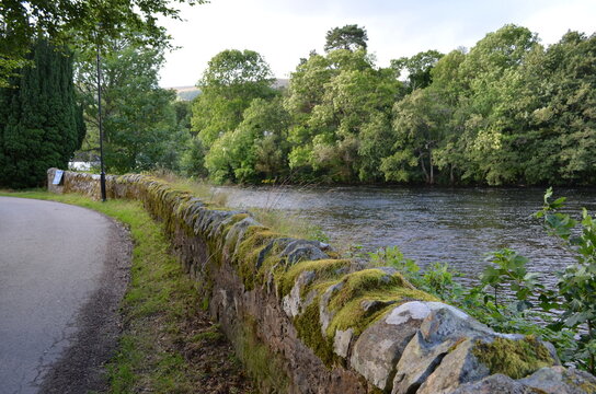 Scenic landscape view of the River Oich flowing next to a traditional mossy stone dyke wall near Fort Augustus, Scotland.
