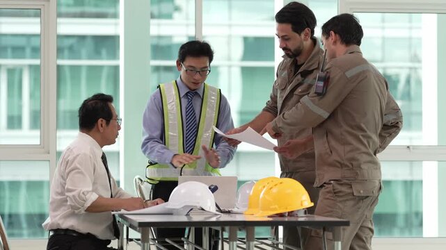 Construction team reviewing building plans around table with safety helmets and reflective vests in office