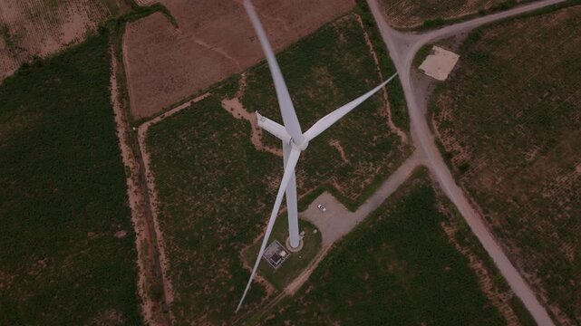 Top down drone view of wind turbine blades rotating over green farmland for clean energy