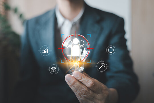 Businessman holding glowing light bulb with people icon and target crosshair. Concept of human resources, recruitment, finding talent, customer targeting, and smart business strategy.