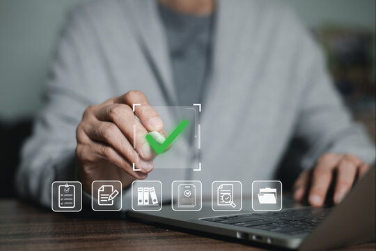 Close up of businessman hand touching virtual green checkmark on digital screen while using laptop. Concept of document approval, quality assurance, compliance, checklist, and online verification.