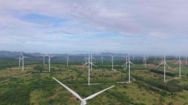 Aerial view of wind turbine blade and wind farm on green hills under blue sky for renewable energy