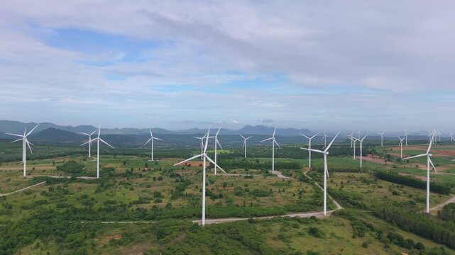 Drone flight over wind farm on green hills with mountains for sustainable clean power