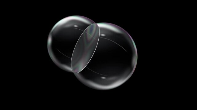 Two soap bubbles drifting together and merging into one large bubble as iridescent wall pops on black