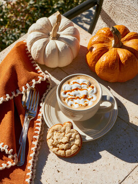 Top down view of a Halloween coffee break with cappuccino, pumpkin cookies, and decorative pumpkins