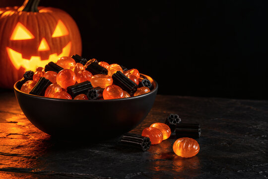 Orange candy and black licorice in a bowl on dark stone