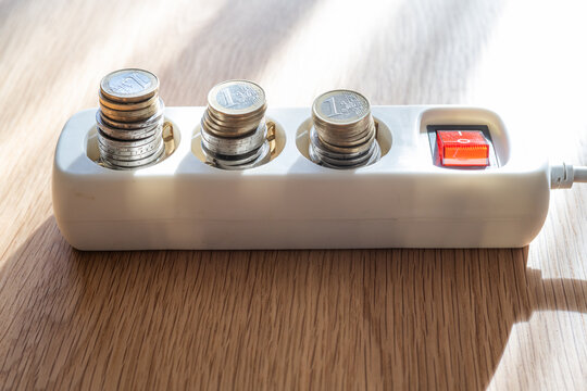 Stacks of euro coins filling power strip sockets, illustrating the concept of increasing electricity consumption costs, energy efficiency, and potential savings