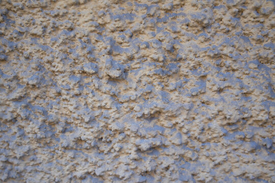 Rough beige and blue-gray plaster wall with an uneven granular surface and abstract texture