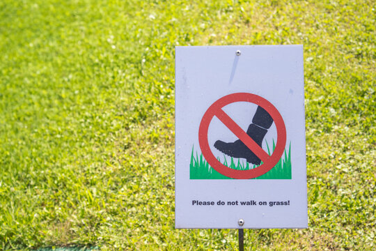Keep off the grass sign with a red prohibition symbol standing on a sunlit green lawn