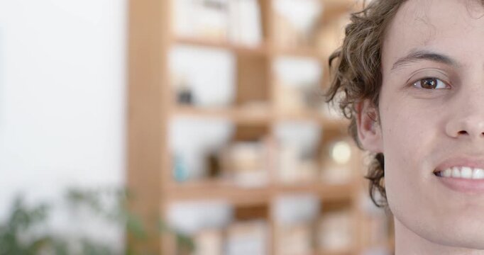 Camera pulling back, man in 20s-30s shifting left, smiling, blinking near shelving, plant at home