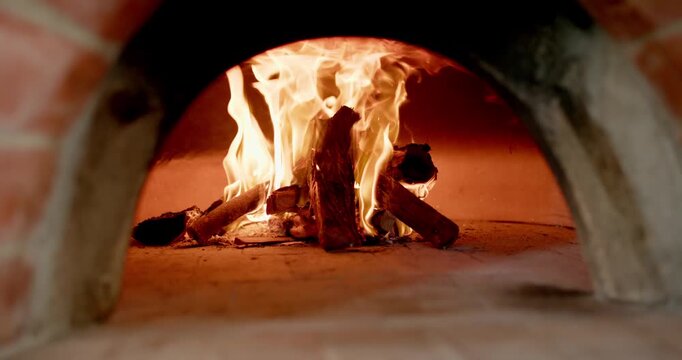 Glowing embers igniting, stacked firewood is burning inside masonry oven, sending heat for baking