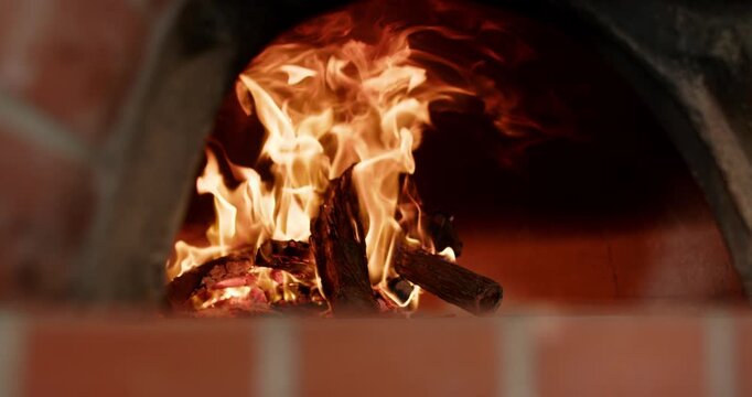 Log stack is burning after ignition, flames are rising, curling in brick oven to heat interior