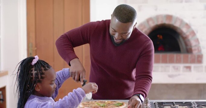 African American dad, child in knits placing cutter on pizza slicing sprinkling on counter to serve