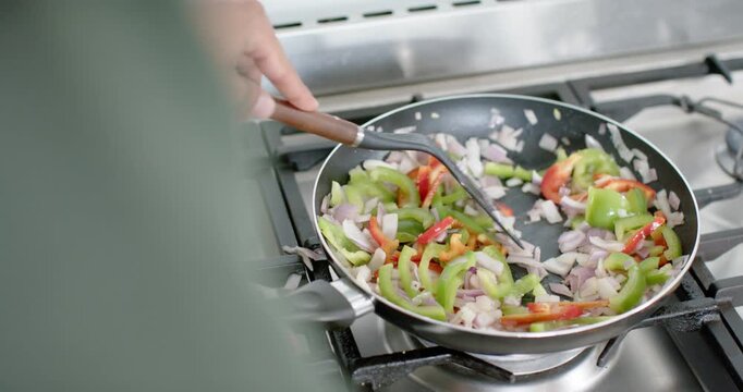 Gas burner igniting is heating pan as cook is stirring peppers and onions to spread evenly