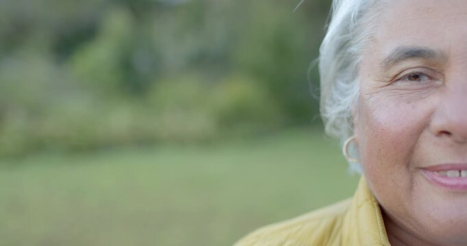 African American senior woman tilting, smiling at camera in park yellow jacket gold hoop
