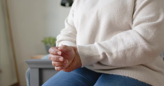 Seated woman is rubbing left wrist and adjusting dark strap after noticing shift in living room