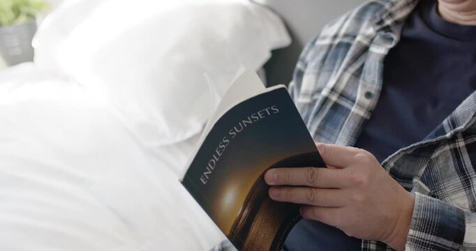 Male reader is opening paperback ENDLESS SUNSETS, flipping pages and settling into reading on bed
