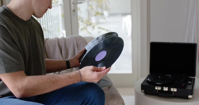 Man sitting on sofa by patio doors choosing vinyl records to play, checking labels